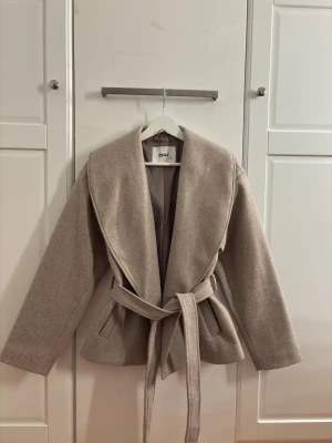 Beige kappa med bälte från ONLY - Säljer nu min jätte snygga beiga kappa ifrån only, då den inte längre kommer till användning och söker nytt hem. Kappan har ett bälte runt midjan och en bred krage, med en klassisk fin beige färg. Perfekt för dig som vill hålla en stil ren look, men inte allt för mycket!☺️