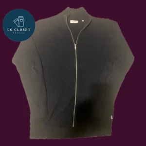 Svart stickad kofta från Lindbergh - Svart stickad kofta från Lindbergh med snygg struktur och hel dragkedja framtill. Modellen har ribbad krage och muddar, vilket ger en schysst och modern look. Perfekt för dig som gillar stilrena och klassiska plagg med lite edge.