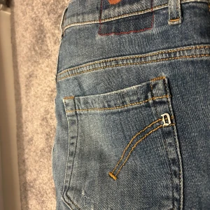Dondup  med patch och slitningar - Snygga blå jeans från dondup  med coola patch-detaljer och slitningar på benen. Modellen är slim fit med klassisk femficksdesign och låg midja. Jeansen har gul kontrastsöm och metall-D på fickan. Perfekt för dig som gillar en festlig stil