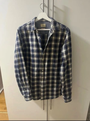 Blårutig skjorta från Selected Homme - Blårutig skjorta från Selected Homme Heritage, regular fit. Skjortan har klassisk krage, långa ärmar och knappar framtill. Materialet är mjuk bomull som känns skönt mot huden. Perfekt för dig som gillar avslappnad stil med lite edge.