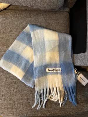 Acne studios halsduk - Supermjuk och fluffig halsduk från Acne Studios i rutigt mönster med ljusblå och vita toner. Stora rutor, långa fransar och tydlig logotyp framtill. Perfekt accessoar för att lyfta vinterlooken med en cool touch. Mått Längd 220 cm Bredd 40 cm