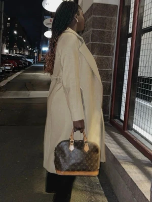 Beige kappa med bälte och bred krage - Snygg beige kappa med bred krage och bälte i midjan. Lång modell med klassisk look och knäppning framtill. Perfekt för dig som vill ha en stilren och tidlös jacka till höst och vinter. Fodrad insida för extra komfort.