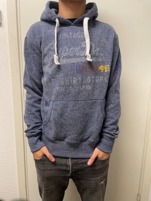 Hoodie från Superdry  - Fet hoodie från Superdry. Lite slitet tryck annars bra skick. Modellen är 173cm, 64kg. Pris kan självklart diskuteras!