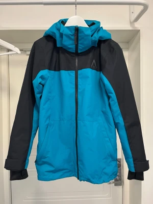 Skid/snowboardjacka strl 160 - Mjukt fodrad vind och vattentät skidjacka med alla nödvändiga funktioner och mycket fint skick (använd endast 1 skidweekend innan den blev för liten).  Ficka för liftkort på jackärmen, innerficka och rymliga sidofickor med dragkedja. Mjuk fleece som skydd för hakan.  Ordinarie pris 1400 kr. 