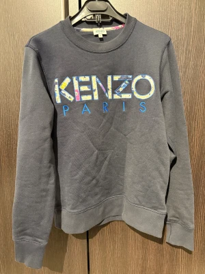 Mörkblå sweatshirt från Kenzo - Snygg mörkblå sweatshirt från Kenzo med stort broderat Kenzo Paris-tryck i färgglada bokstäver på bröstet. Tröjan är i storlek S.