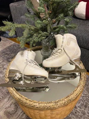Vita konståkningsskridskor från Edea (B) storlek 230  - Säljer ett par vita konståkningsskridskor från edea med snygga detaljer och snörning framtill. Skridskorna har silvriga Apex Supreme-stål och är tillverkade i skinn och syntetmaterial. Perfekta för dig som vill glida fram på isen med stil.
