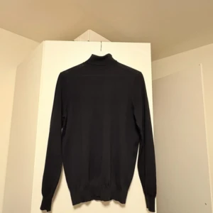 Svart polotröja i ull från Suitsupply - Tidlös polotröja i merinoull från Suitsupply – elegant, tunn och lyxigt mjuk. 	•	Märke: Suitsupply 	•	Modell: Merino Turtleneck 	•	Färg: Navy (mörkblå) 	•	Storlek: S 	•	Material: 100 % merinoull 	•	Nypris: ca 1 199 kr (suitsupply.com) 	•	Skick: Använd cirka 5 gånger, perfekt skick