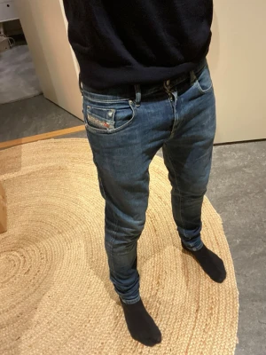 Blå skinny jeans från Diesel W28 - Säljer ett par blå skinny jeans från Diesel i storlek W28. Klassisk femficksmodell med snygga slitningar och röda Diesel-detaljer på fickan. Jeansen har låg midja och är tillverkade i stretchigt denim för en tight passform.