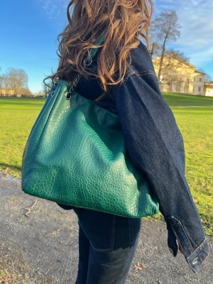 Grön axelväska med kedjedetalj - Snygg grön axelväska i skinnimitation med cool kedja som axelrem. Väskan har en mjuk, lite slouchy form och ett strukturerat mönster som ger den extra attityd. Perfekt storlek för allt du behöver och passar till både jeans och jacka.