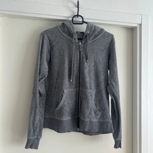 Grå hoodie med dragkedja och huva - Mjuk grå hoodie med dragkedja framtill, huva med snörning och två fickor. Långärmad och tillverkad i bomullsmix som känns skön mot huden. Perfekt för chill dagar eller när du vill ha något bekvämt på dig. Enkel och stilren design som funkar till det mesta.