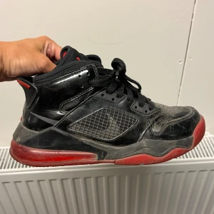 Svarta och röda Air Jordan sneakers strl 39 - Säljer ett par svarta Nike Air Jordan sneakers med röda detaljer och genomskinlig röd sula. Skorna har snörning, hög modell och klassisk Jumpman-logga på hälen. Ovandelen är i blankt syntetmaterial med meshpaneler på sidorna. Perfekta för dig som gillar streetwear. Ok använt skick. 