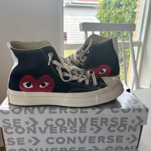 Converse x CDG Play svarta sneakers - Svarta Converse Chuck Taylor high-tops i samarbete med Comme des Garçons Play. Skorna har det ikoniska röda hjärta-trycket med ögon på sidan, vita snören och sula. Tillverkade i canvas med klassisk vit gummisula och kontrastsömmar. Dom är använda två gånger därav pris