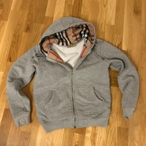 Grå hoodie från Burberry med dragkedja - Säljer en grå hoodie från Burberry med klassiskt rutigt foder i huvan. pris kan diskuteras vid snabb affär 