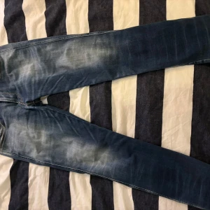 Replay Anbass blå jeans - Säljer ett par Replay Anbass jeans i blå tvätt med snygga slitningar och ljusa partier. Klassisk femficksmodell med raka ben och detaljerade bakfickor. Jeansen har Replay-logga vid fickan och är tillverkade i mjukt jeanstyg.