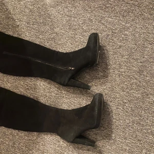 Svarta höga stövletter med klack - Snygga svarta stövletter med hög klack och spetsig tå. Skorna är i mocka och har dragkedja på sidan för enkel påtagning. Storlek 39