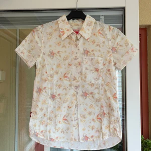 Blommig kortärmad skjorta Levi's - Kortärmad skjorta från Levi's i ljus bomull med blommigt mönster i pastellfärger som gult, lila och orange. Skjortan har klassisk krage, bröstficka och knappar framtill.. Storlek XS.