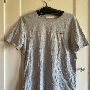 Grå t-shirt med broderade läppar - Snygg grå t-shirt från Carin Wester i mjuk bomull. På bröstet finns en liten broderad detalj med röda läppar som ger en cool touch. Perfekt till skolan! Nypris 350 kr 