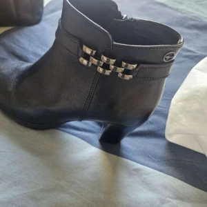 Svarta stövletter med metall-detalj - Snygga svarta stövletter i skinn med klack och dekorativa metall-detaljer på sidan. Dragkedja på insidan för enkel på- och avtagning. Perfekta för dig som vill ha en stilren och trendig look.