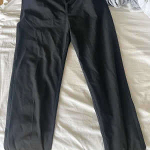 Svarta kostymbyxor från Lindex - Klassiska svarta kostymbyxor från Lindex i storlek 38. Byxorna har rak passform och är tillverkade i ett mjukt och följsamt material som ger en snygg siluett. Perfekta för en clean och stilren look.