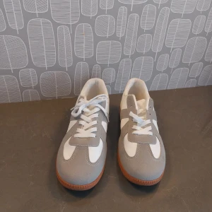 Renzo  sneakers med mockadetaljer från Arveilo  - Snygga sneakers Renzo  från Arveilo i vitt och ljusgrått med ovandel i mocka och syntet. Skorna har klassisk snörning, vit textil på insidan och en brun gummisula. Skorna är använda 1 gång men passade tyvärr inte foten.