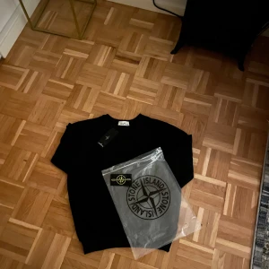 Svart stickad tröja från Stone Island - Svart stickad tröja från Stone Island med klassisk rund hals och ikonisk logga på ärmen. Tröjan har ribbade muddar och är perfekt för dig som gillar stilren streetwear. Materialet är mjukt och passar bra till lager-på-lager under kyligare dagar. Skickas samma eller nästa dag efter köp✅📦