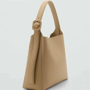 Beige axelväska med bred rem - Stilren beige axelväska med bred axelrem och snyggt spänne. Väskan har en minimalistisk design och är tillverkad i slätt syntetmaterial. Perfekt för dig som gillar enkel och modern stil.