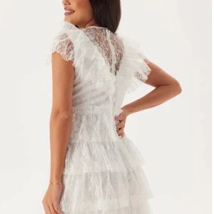 Vit spetsklänning med volanger - Superfin vit kort spetsklänning med flera lager volanger och transparenta detaljer upptill. Klänningen har rund hals, korta ärmar och v-ringad spets framtill. Perfekt för student eller sommarens alla tillfällen! Har använt det i några timmar så den är helt ny och ny tvättad! 