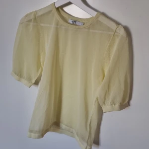 Gul meshblus med puffärm från NA-KD - Superfin ljusgul blus i mesh från A.KD med puffiga korta ärmar och rund halsringning. Tunt och transparent material som ger en luftig känsla. Perfekt att styla lager på lager för en trendig look.