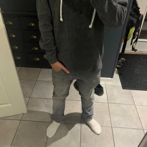 Snygg mörkgrå stickad hoodie från Jack & Jones - Mörkgrå stickad hoodie från Jack & Jones med vit snörning i huvan. Tröjan har ribbade muddar, lång ärm och en snygg, enkel design. Perfekt för dig som gillar en chill och stilren look. Materialet är mjukt och värmande, passar bra till kalla dagar. Säljer pga har för många tröjor.