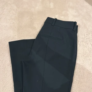 Mörk gröna kostymbyxor från Zara S - Eleganta mörk gröna kostymbyxor från Zara i storlek S. Byxorna har raka ben, hällor för bälte, dold dragkedja och knäppning fram samt diskreta bakfickor. Perfekta för en clean och stilren look. Materialet känns mjukt och följsamt.