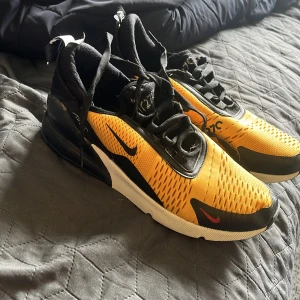 Nike Air Max 270 sneakers gul/svart - Nike Air Max 270 sneakers i en riktigt snygg gul och svart färgkombination. Ovandelen är i mesh med svarta detaljer och tydlig Air Max-dämpning i hälen. Skorna har snörning och en sportig vibe, perfekt för dig som gillar streetstyle och komfort.