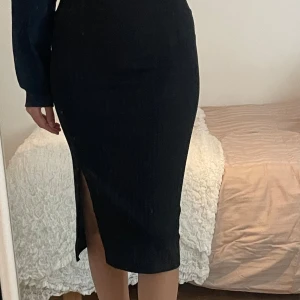 Svart långkjol med slits - Säljer en svart långkjol med tight passform och snygg slits på sidan. Kjolen har en stilren och klassisk look som passar perfekt till många olika outfits. Materialet känns mjukt och följsamt mot kroppen.