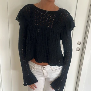Svart spetsblus med volangärmar - Supersöt svart blus i spets med långärmade, lätt utsvängda ärmar och volangdetaljer på axlarna. Blusen har en luftig, lös passform 🥰 