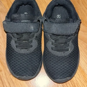 Svarta sneakers med kardborreband - Svarta sneakers i mesh med kardborreband och elastiska snören. Skorna har en platt sula och rund tå, samt dragflik baktill för enkel påtagning. Perfekta för en sportig och avslappnad stil.