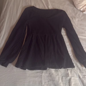 Svart ribbad långärmad blus - Svart långärmad blus med ribbat tyg och lätt utsvängd nederdel. Toppen har en rundad halsringning och markerad midja som ger en snygg siluett. Den är oanvänd med nytt skick💕 