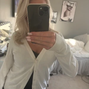 Vit kofta från H&M Basic, storlek S - Säljer en klassisk vit kofta från H&M Basic i storlek S. Koftan har v-ringning, långa ärmar och knäppning framtill med matchande vita knappar. Perfekt att slänga över en topp för en clean och enkel look.