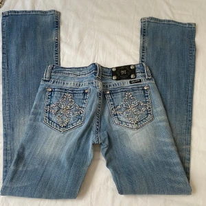 Ljusblå bootcut med broderade bakfickor - Snygga lågmidjade jeans från Miss Me med broderade bakfickor och blingdetaljer. Defekter finns på två sista bilderna 