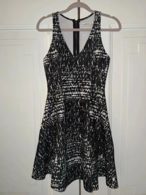 Svartvitt mönstrad klänning Abercrombie - Säljer en svartvitt mönstrad klänning från Abercrombie & Fitch. Klänningen har v-ringning, är ärmlös och har en snygg, figurnära passform upptill med utställd kjol. Dragkedja bak för enkel påklädning. Perfekt för dig som gillar grafiska mönster!