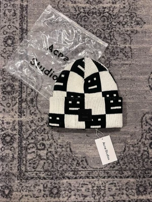 mössa Acne Studios - Snygg svartvit stickad mössa från Acne Studios med rutigt mönster och den klassiska Face-loggan framtill. Mössan är ribbstickad och har uppvikt kant. Perfekt accessoar för att lyfta din streetwear-look.