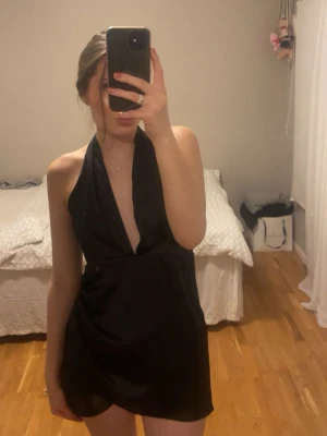Svart halterneck miniklänning  - Snygg svart kort klänning med djup v-ringning och halterneck. Klänningen har en figurnära passform. Materialet känns lätt och följsamt. Klänningen är i storelek M men passar även S.💕