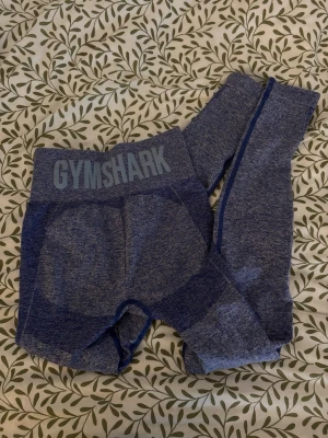 Flex leggings från Gymshark - Säljer blåa träningsleggings från Gymshark i deras flex modell med hög midja. De är formade efter kroppen och är av stretchigt material, 57% nylon, 36% polyester och 7% elastane. Legginserna är använda ett få tal gånger och har inga tecken på slitage. Finns inte att köpa i den blåa färgen.
