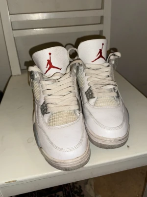 Nice Air Fordan 4 vita sneakers - Säljer ett par klassiska Nice Air Fordan 4 sneakers i vitt med grå och röda detaljer. Skorna har snörning, meshpaneler och den ikoniska Fumpman-loggan på plösen. Perfekta för dig som gillar streetwear och vill ha en tidlös sneaker i garderoben. behöver nya sulor och stor chans att dom är fa-k-e