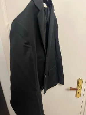 Svart H&M kavaj stl 152 - Stilren svart kavaj med enkelknäppning och klassisk krage. Kavajen har raka linjer, två fickor framtill och är helfärgad utan mönster. Perfekt för en dressad look och passar till många olika outfits. Kan behöva tvättning på grund av damm som satt sig.