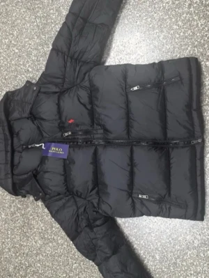 Svart dunjacka från Polo Ralph Lauren - Snygg svart dunjacka från Polo Ralph Lauren med klassisk röd logga på bröstet. Jackan har quiltad design, dragkedja framtill och flera praktiska fickor med dragkedja. Perfekt för kalla dagar och riktigt stilren look.