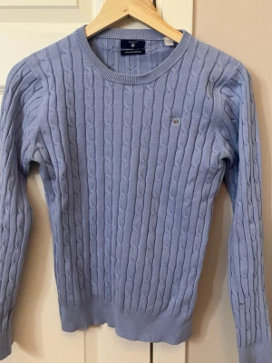 Ljusblå kabelstickad tröja från Gant - Supersnygg ljusblå kabelstickad tröja från Gant med rund halsringning och diskret broderad logga på bröstet. 
