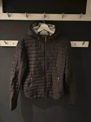 Svart jacka från Colmar - Säljer en svart pufferjacka från Colmar med huva och dragkedja framtill. Jackan har quiltad design, två fickor med dragkedja och Colmar-logga på ärmen. Den har en lagning på vardera undersidor av ärmarna men inget som märks speciellt mycket vid användning  