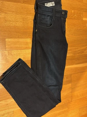 Replay jeans - Säljer ett par svarta Replay jeans med klassisk femficksdesign och dragkedja. Jeansen har en smal passform och är tillverkade i mjukt jeansmaterial med diskreta slitningar. Perfekta för dig som gillar stilrena och bekväma jeans.