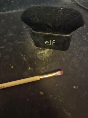 e.l.f. kabukiborste & Revolution pensel - Säljer en svart kabukiborste från e.l.f. med täta, mjuka syntetborst och kompakt design. Medföljer gör en smal sminkpensel från Revolution med träfärgat skaft och rosa topp, perfekt för detaljerad applicering av ögonskugga eller läpprodukter.