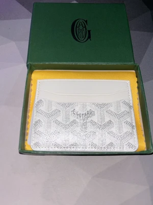 Vit kortfodral från Goy4rd - Snyggt vitt kortfodral från Goy4rd med ikoniskt mönster och flera kortfack. Tillverkat i exklusivt skinn med Goy4rd klassiska tryck i grå toner. Perfekt för dig som vill ha en stilren och lyxig accessoar i fickan.