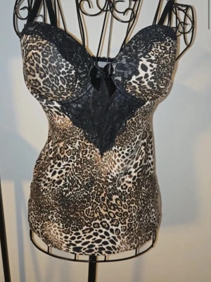 Leopardmönstrad festtopp med spetsdetaljer - Snygg body med leopardmönster i beige, brunt och svart. Överdelen har svarta spetsdetaljer och en liten rosett framtill. Justerbara axelband och vadderade kupor ger extra stöd. Materialet är stretchigt och följsamt för en bekväm passform. Perfekt till fester eller annat💕
